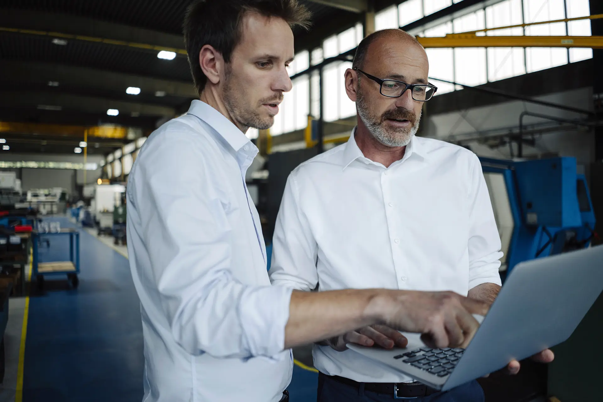 Two managers reviewing a program schedule on a laptop on the shop floor
