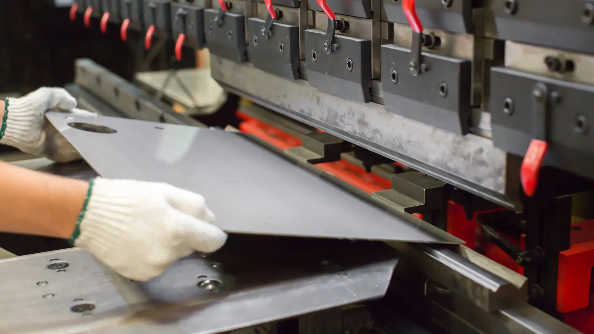 Precision metalwork on the shop floor, a gloved operator setting a part into the press