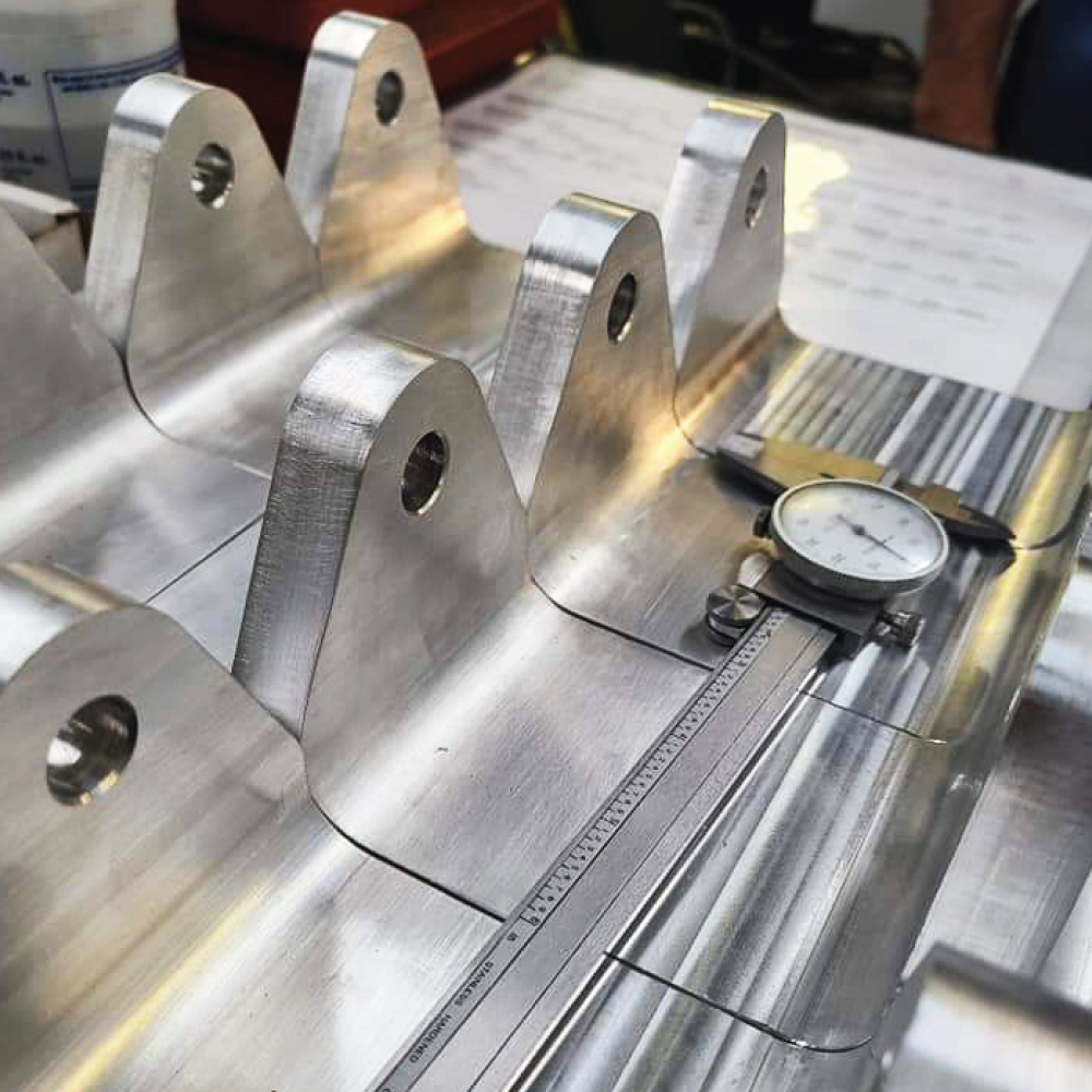 Machined aluminum brackets being measured with a dial caliper and steel rule against the drawing